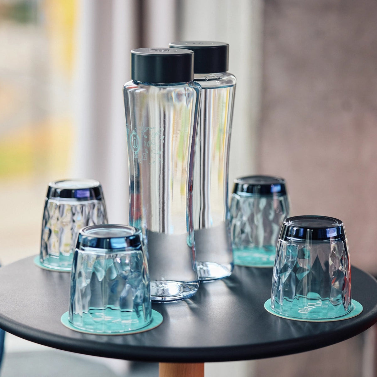 Bottiglie BRITA Twist con tappi neri appoggiate su un tavolo rotondo nero.