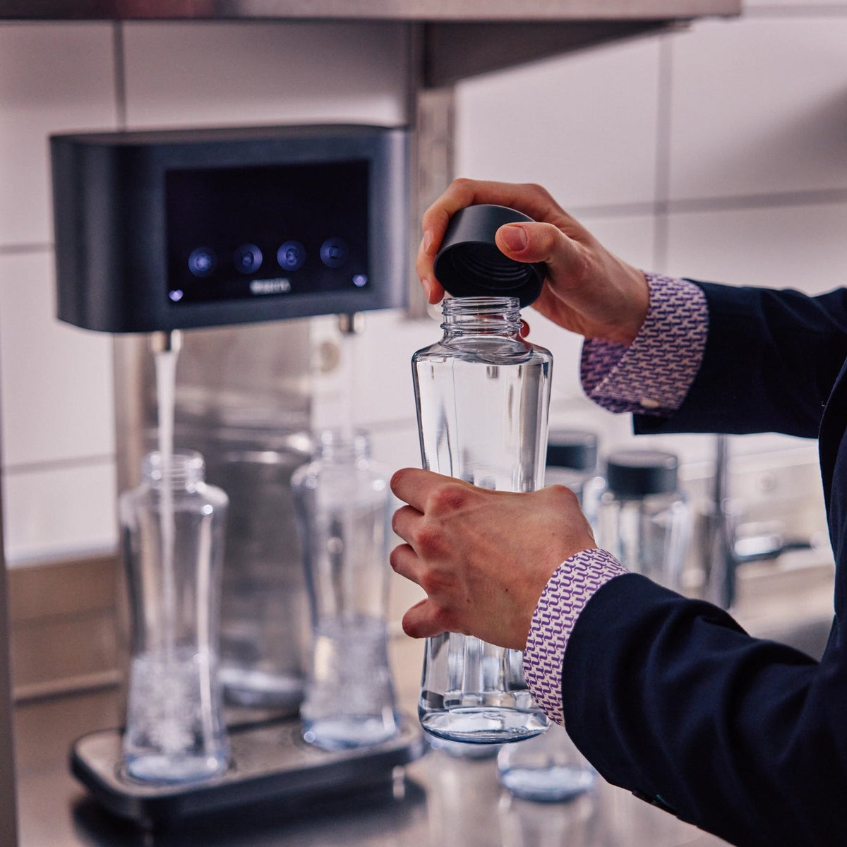 Persona che tiene in mano un BRITA Bottiglia Twist con un tappo scuro davanti a un BRITA Fill T-Tap.