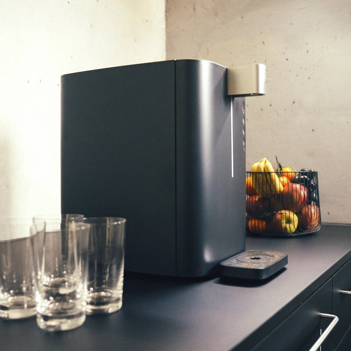 BRITA Top Compact sul piano di lavoro della cucina, con dei bicchieri e un cesto di frutta sullo sfondo.