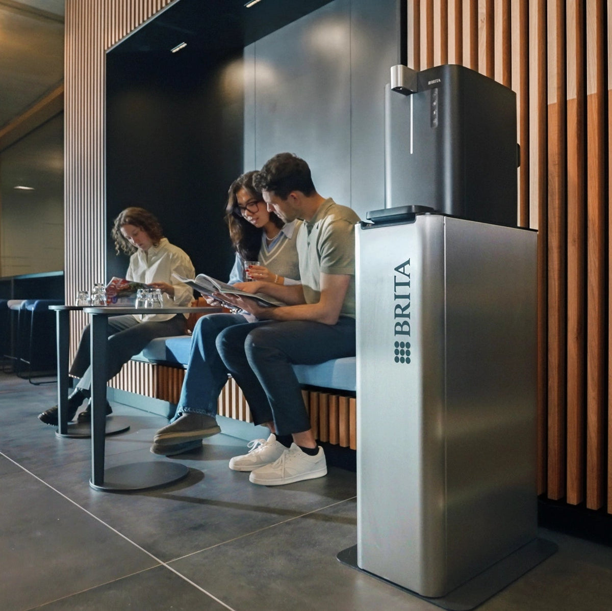 Persone sedute in un moderno ambiente d'ufficio accanto a un distributore d'acqua BRITA Top Compact.